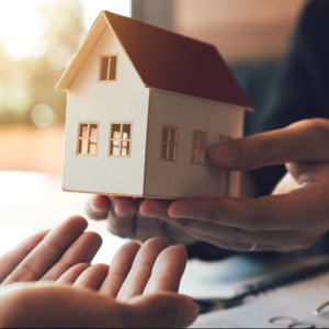 Hands holding a miniature house model, symbolizing home inspection and ownership.