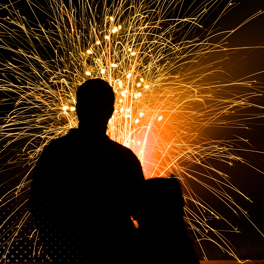 Person silhouetted against a backdrop of bright, colorful fireworks at night