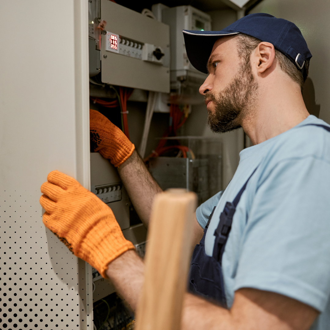 A home inspector inspector, equipped with safety gloves and a cap, inspects the wiring inside an electrical box.