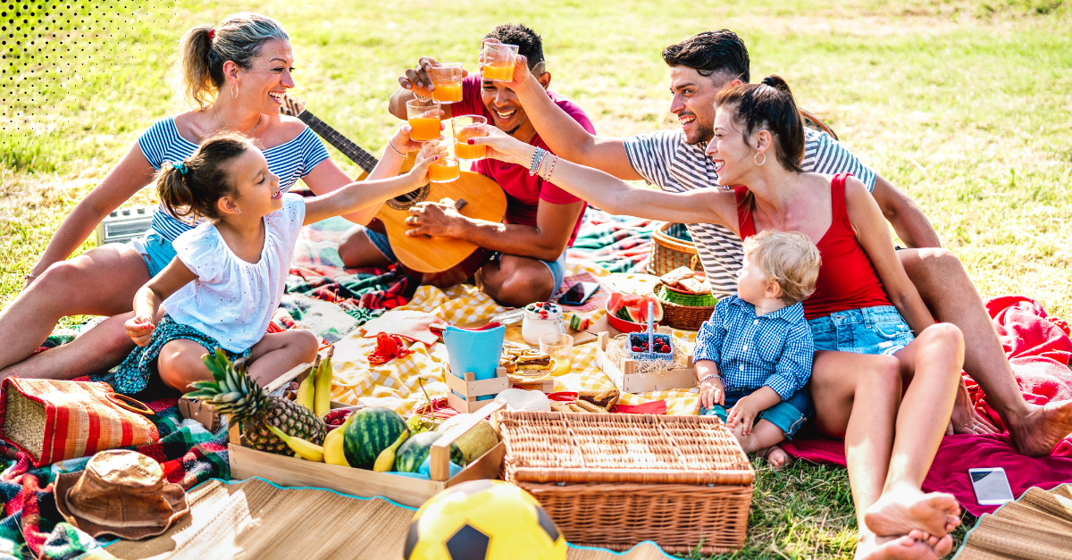 Two families enjoying a lively outdoor picnic with food and drinks, creating joyful fall memories together.