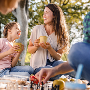 Mother and daughter sharing a laugh while enjoying hot drinks outdoors with family