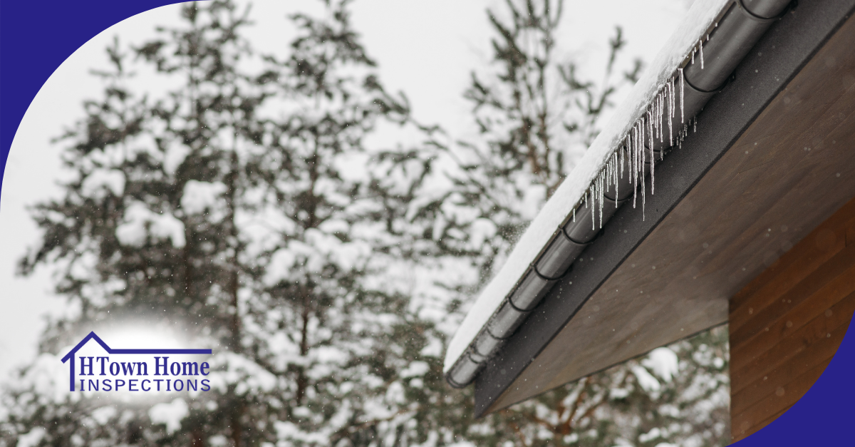 Icicles hanging from a snow-covered roof edge with snowy trees in the background.