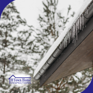 Icicles hanging from a snow-covered roof edge with snowy trees in the background.