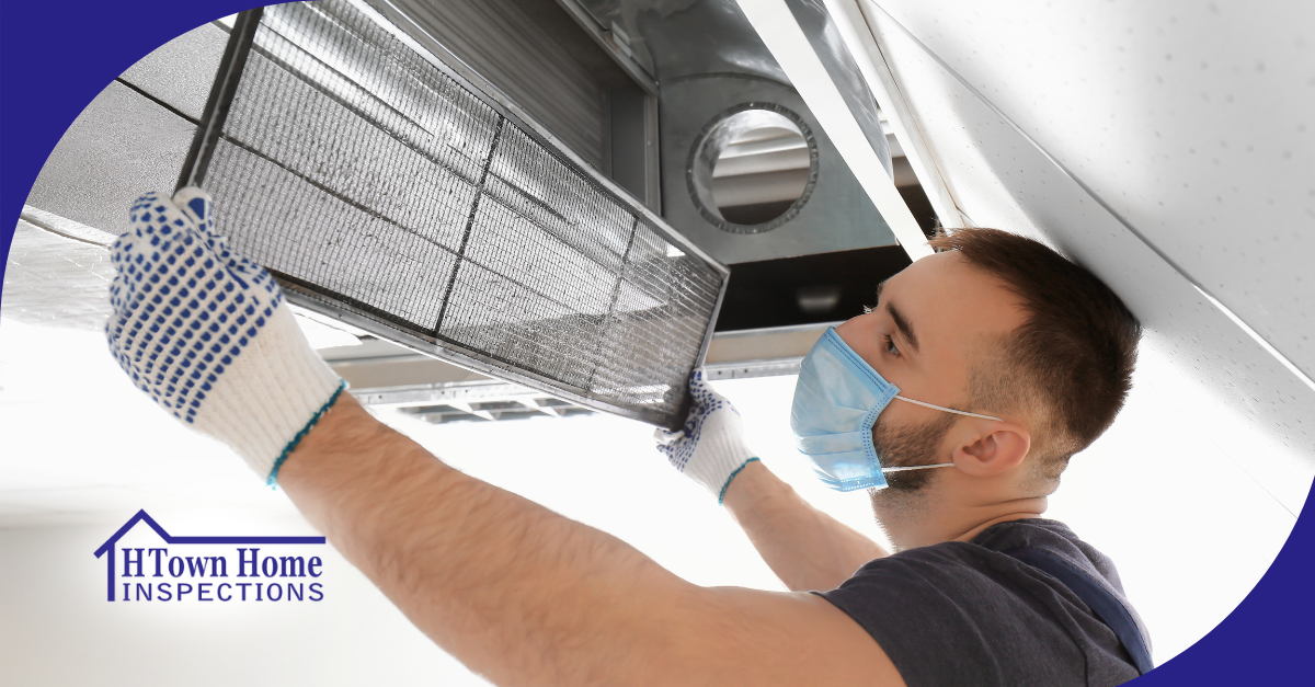 A technician wearing a protective face mask and gloves inspects or replaces an air filter in an HVAC system.