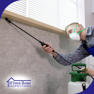 Pest control technician wearing protective gear spraying pesticide along a wall indoors.