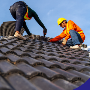 Two roof inspectors installing roof tiles with safety gear on a clear day.