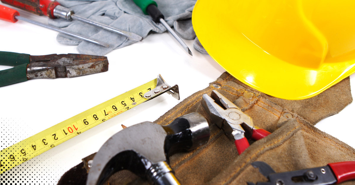 Assorted hand tools with a yellow hard hat and tool belt laid out on a white background.