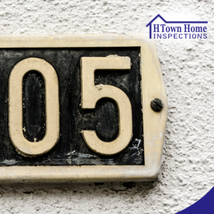 House number 105 on a beige and black metal plaque mounted on a wall.