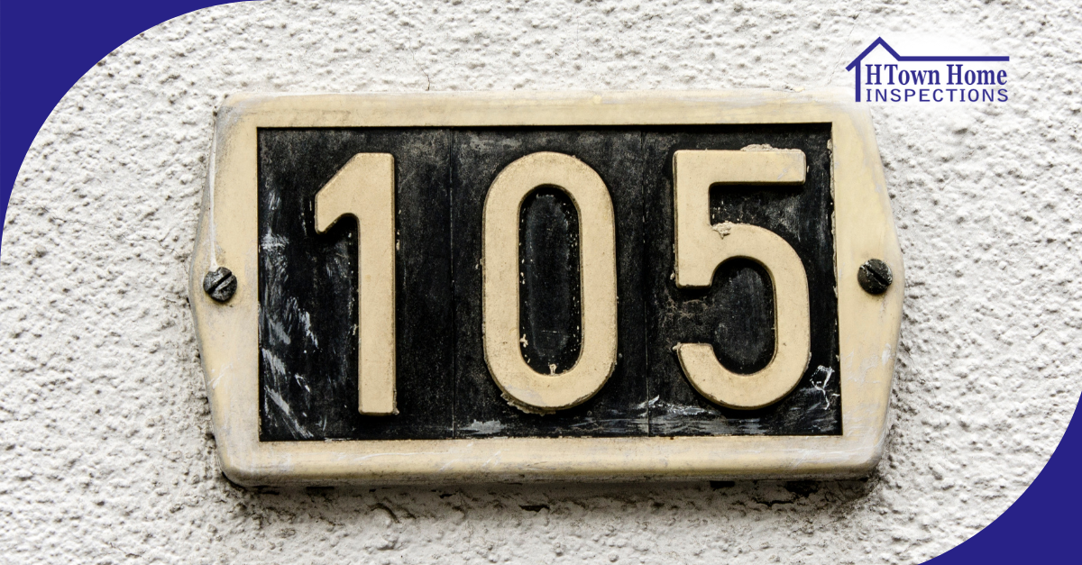 House number 105 on a beige and black metal plaque mounted on a wall.