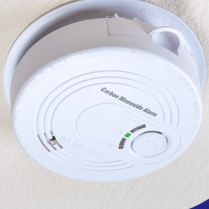 A carbon monoxide alarm on the ceiling with a green indicator light