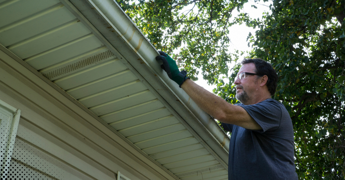 Man inspecting and cleaning a home’s gutter.